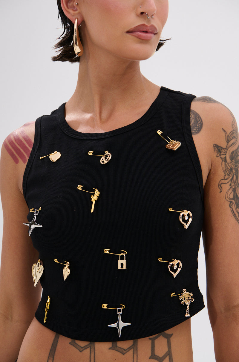 A person wears the LOVIN' YOU EMBELLISHED TANK TOP with black racerback style, gold safety pins, and gold charms. They also have tattoos on their arm and shoulder, a gold earring, and a nose ring. 6