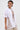 Wearing the SLASHED UP OVERSIZED SHORT SLEEVE TEE with bold horizontal cutouts over beige pants, this look is finished with hoop earrings, layered necklaces, and slicked-back hair against a simple background.