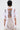 A person with short dark hair wears the SLASHED UP OVERSIZED SHORT SLEEVE TEE featuring horizontal slits down the back, revealing a tattoo. They pair it with a beige skirt and carry a white handbag.