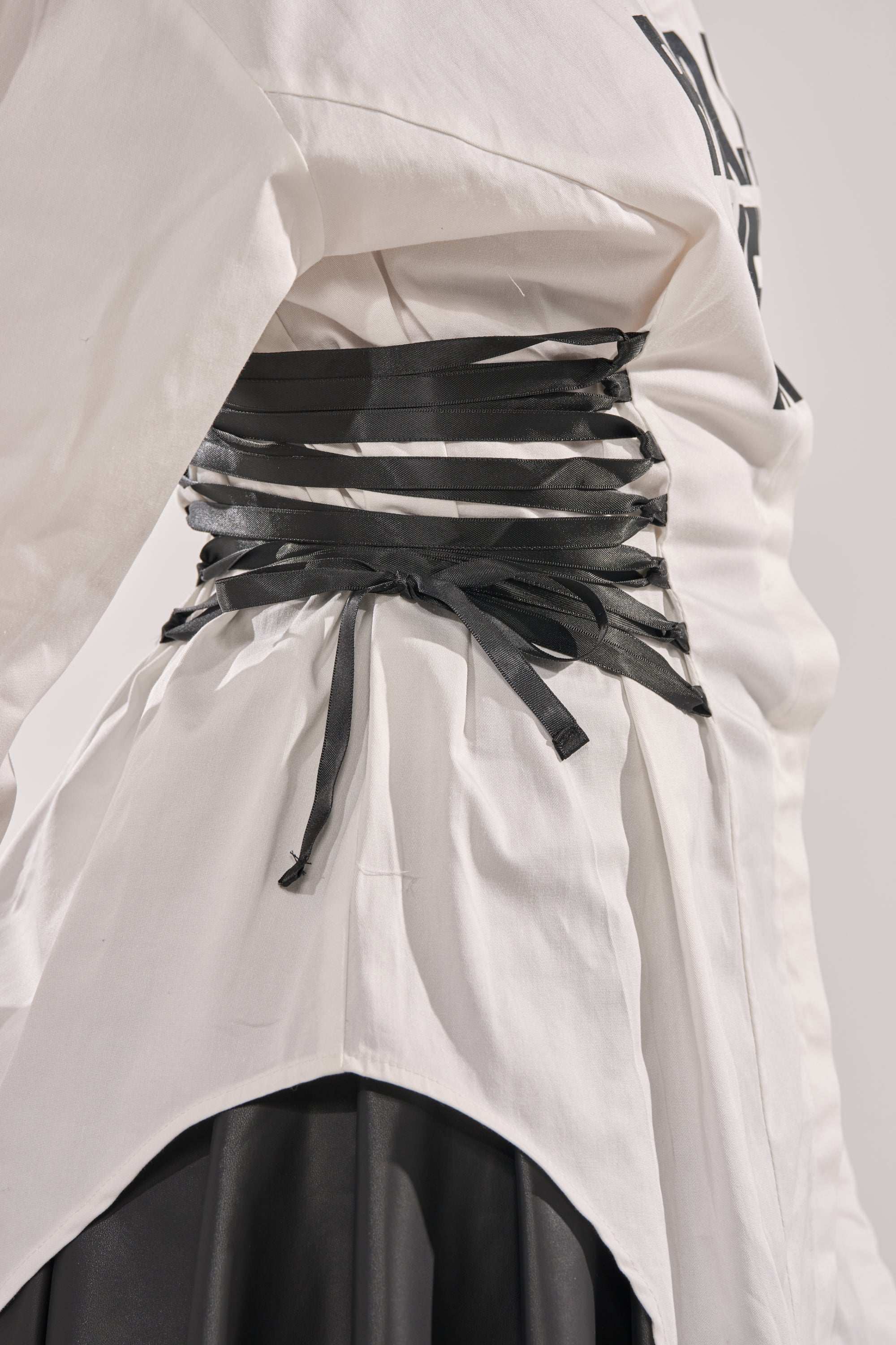 A close-up of a person wearing the REALLY HER POPLIN BLOUSE, cinched at the waist with multiple black leather straps in a crisscross pattern over a black skirt. 7