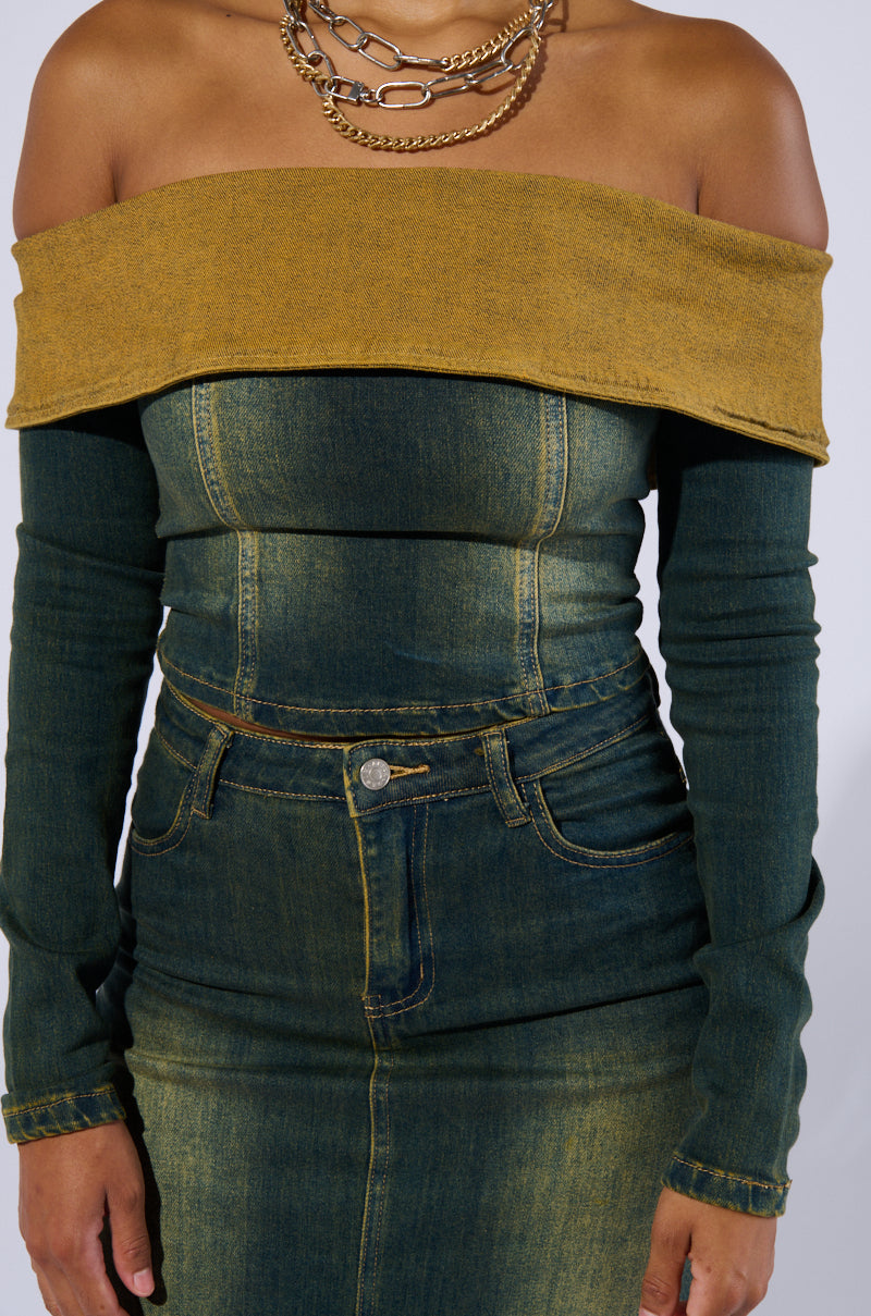 A person wearing the BEFORE YOU GO OFF THE SHOULDER DENIM TOP, which features long sleeves and is paired with a matching high-waisted denim skirt. The Y2K-inspired finish gives the denim fabric a slightly worn, vintage look. They are accessorized with layered gold chains around their neck.