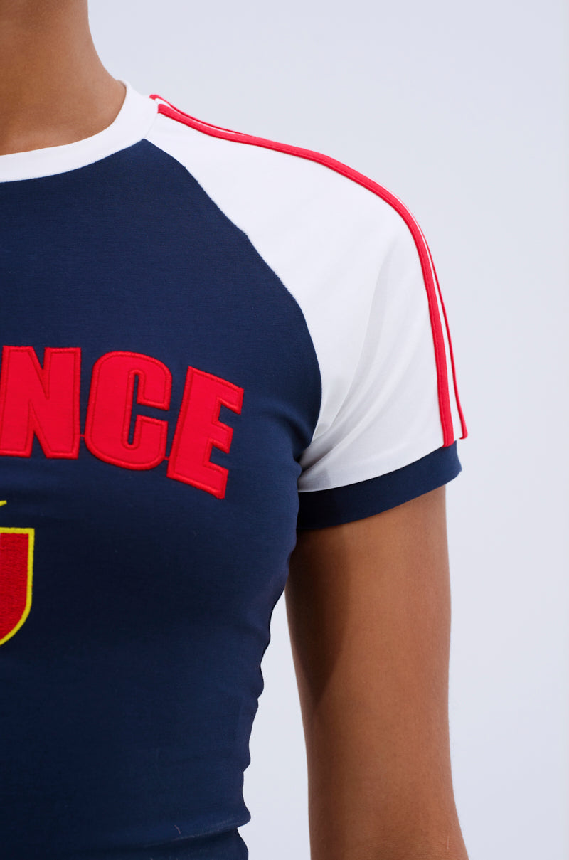 A person wears the FRANCE BABY TEE, a navy and white cotton color block style featuring red shoulder stripes and partial "FRANCE" lettering on the chest.