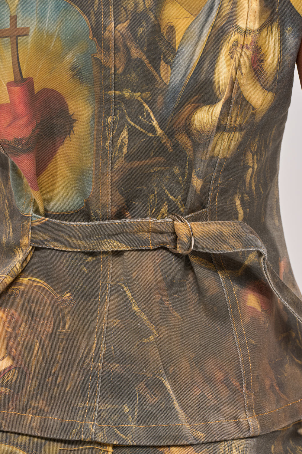 Close-up of the AMEN TO THAT BUTTON DOWN, a baroque-printed denim top with religious imagery like a sacred heart and praying figure. This streetwear style features visible stitching and a fabric belt with metal ring. 9