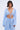 A woman with short dark hair wears the ICED OUT TIE FRONT TOP, a light blue, textured piece with a deep V neckline and boho vibe. She pairs it with matching high-waisted pants and stands confidently against a plain background.