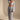 A woman models the ICED OUT PALAZZO PANT, a light blue textured wide-leg pant, paired with a matching long-sleeve cropped top featuring a deep V-neck and tie front. She completes the look with sandals and statement earrings against a neutral backdrop.