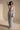 A woman models the ICED OUT PALAZZO PANT, a light blue textured wide-leg pant, paired with a matching long-sleeve cropped top featuring a deep V-neck and tie front. She completes the look with sandals and statement earrings against a neutral backdrop.