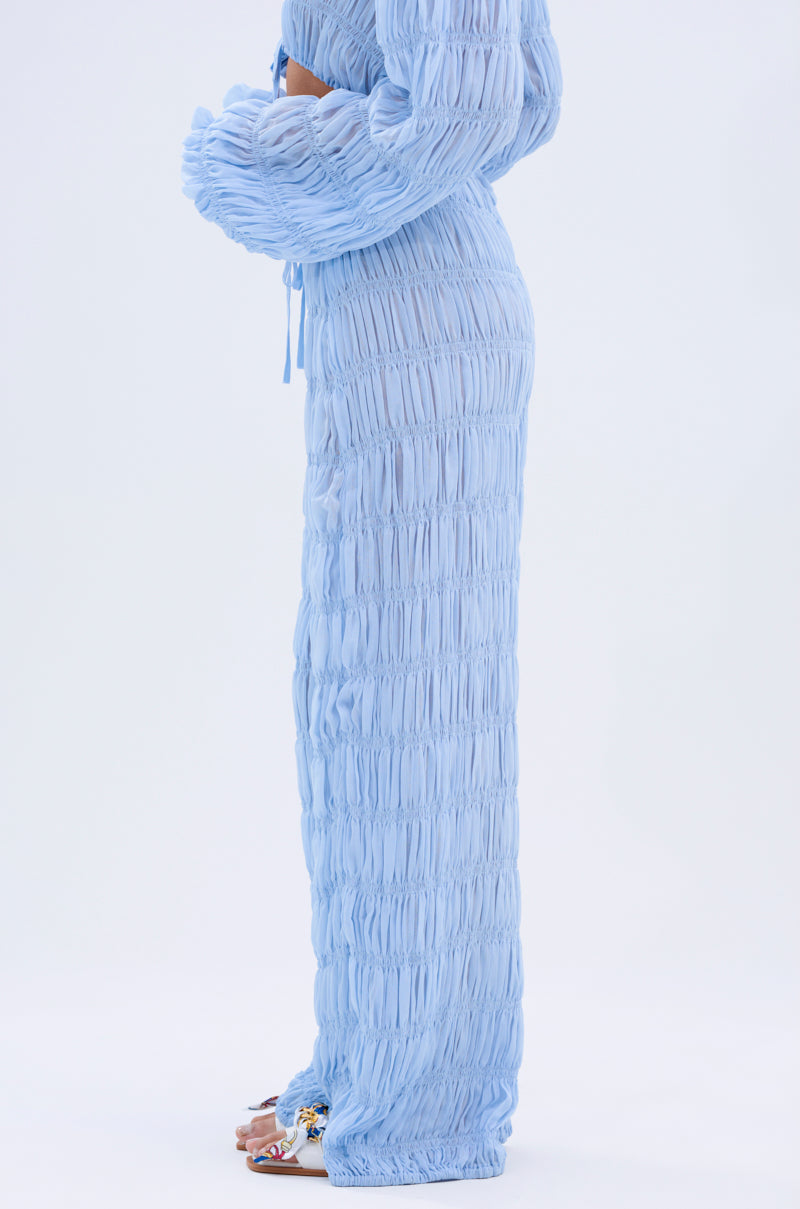 A person stands sideways in a light blue, textured, long-sleeved top and the ICED OUT PALAZZO PANT. They wear open-toed, decorated shoes against a plain white background, creating a subtle boho vibe.