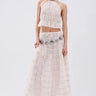 A woman poses against a plain light background in the JUST KEEP GOIN MAXI SKIRT and matching sheer white halter crop top with seersucker detail, styled with a silver concho belt, white boots, and minimal makeup.