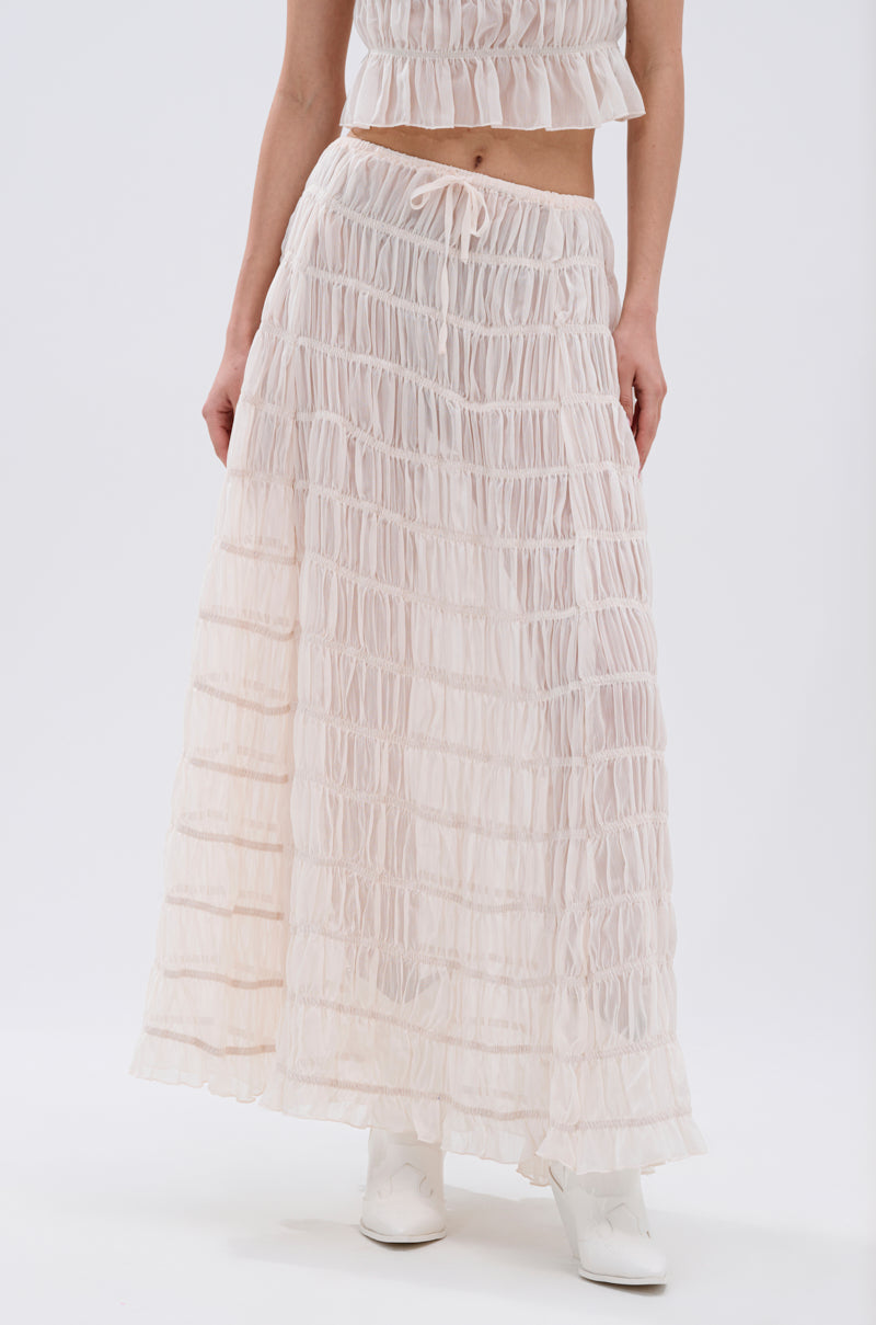 A person wears the JUST KEEP GOIN MAXI SKIRT—a sheer, ruffled, light-toned skirt with subtle seersucker details—plus a matching cropped top and white shoes, standing against a plain white background.