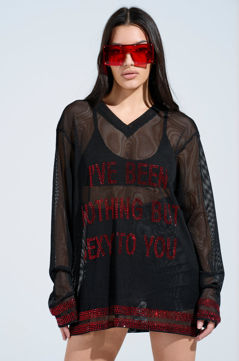 A woman with long dark hair wears large red sunglasses and a sheer black top named "I HAVE BEEN NOTHING BUT SEXY TO YOU JERSEY" with rhinestone text. She stands against a light blue background.