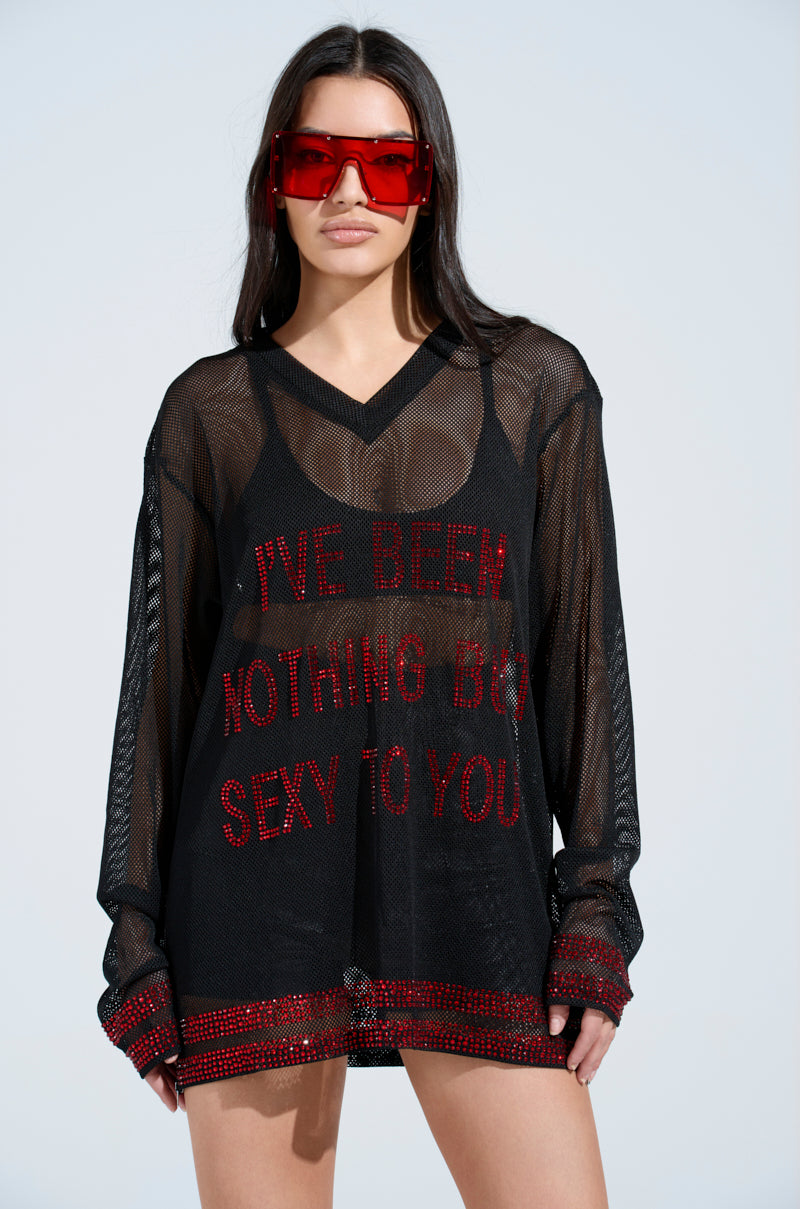Wearing the oversized "I HAVE BEEN NOTHING BUT SEXY TO YOU JERSEY," featuring red text on black mesh, a person with long hair beneath large red sunglasses glows as subtle rhinestone accents catch the light against a minimalist background.
