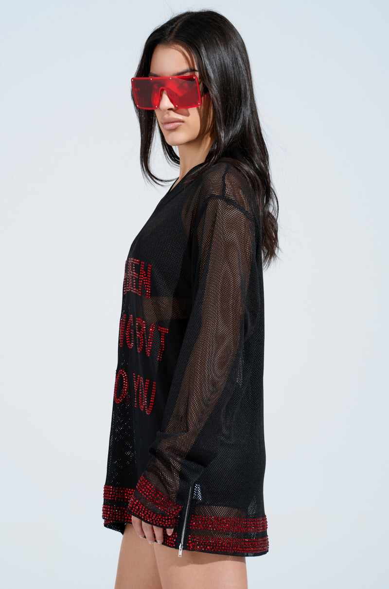 A woman with long dark hair wears red oversized sunglasses and the "I HAVE BEEN NOTHING BUT SEXY TO YOU JERSEY" in black mesh with red trim, featuring rhinestone embellishments. The shirt's oversized silhouette is highlighted as she stands in profile against a light plain background.