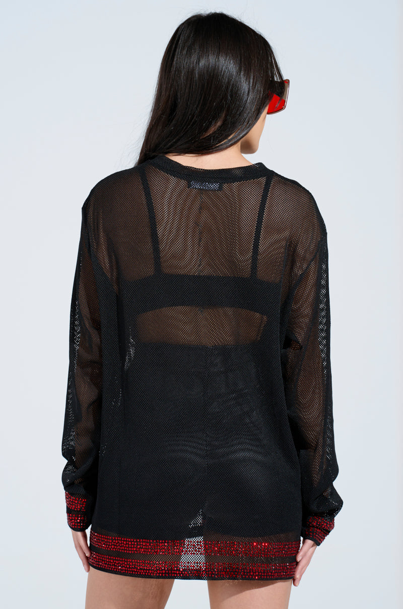 A person with long dark hair wears the "I HAVE BEEN NOTHING BUT SEXY TO YOU JERSEY," featuring a sheer black mesh design, red sequined cuffs and hem, and rhinestone embellishments on the back. They pair it with red sunglasses while facing away to highlight the outfit.