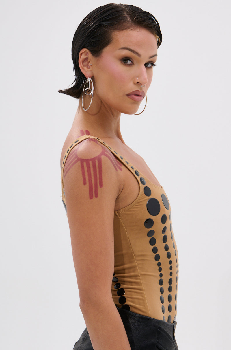 A person with short dark hair, hoop earrings, and pink eyeshadow wears the NOT WHAT YOU THOUGHT POLKA DOT MESH BODYSUIT, featuring sheer mesh with glossy black polka dots. They have a pink drip design on their shoulder against a white background.