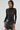 Wearing the NOT MY FAULT LONG SLEEVE MESH BODYSUIT in black with circular patterns, a person pairs it with a short leather skirt. Reflective details enhance their look as they pose against a plain background, long hair cascading down.