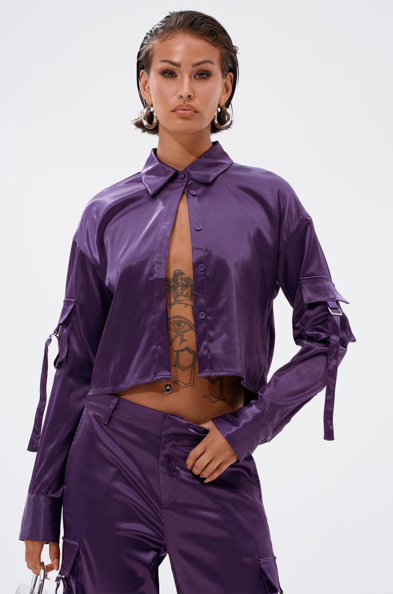 A woman poses confidently in the MAYBE ITS YOU SATIN BUTTON DOWN and matching pants. She has slicked-back hair, hoop earrings, visible torso tattoos, and stands against a plain white background.