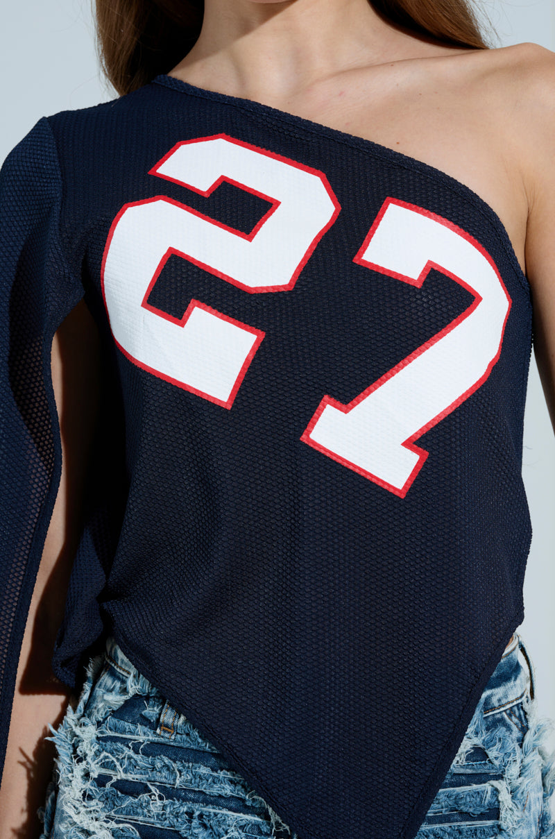 A person sporting the GAME TIME JERSEY in navy blue, featuring an asymmetrical silhouette and number 27 in white and red, completes their sporty-chic look with distressed denim shorts. 7