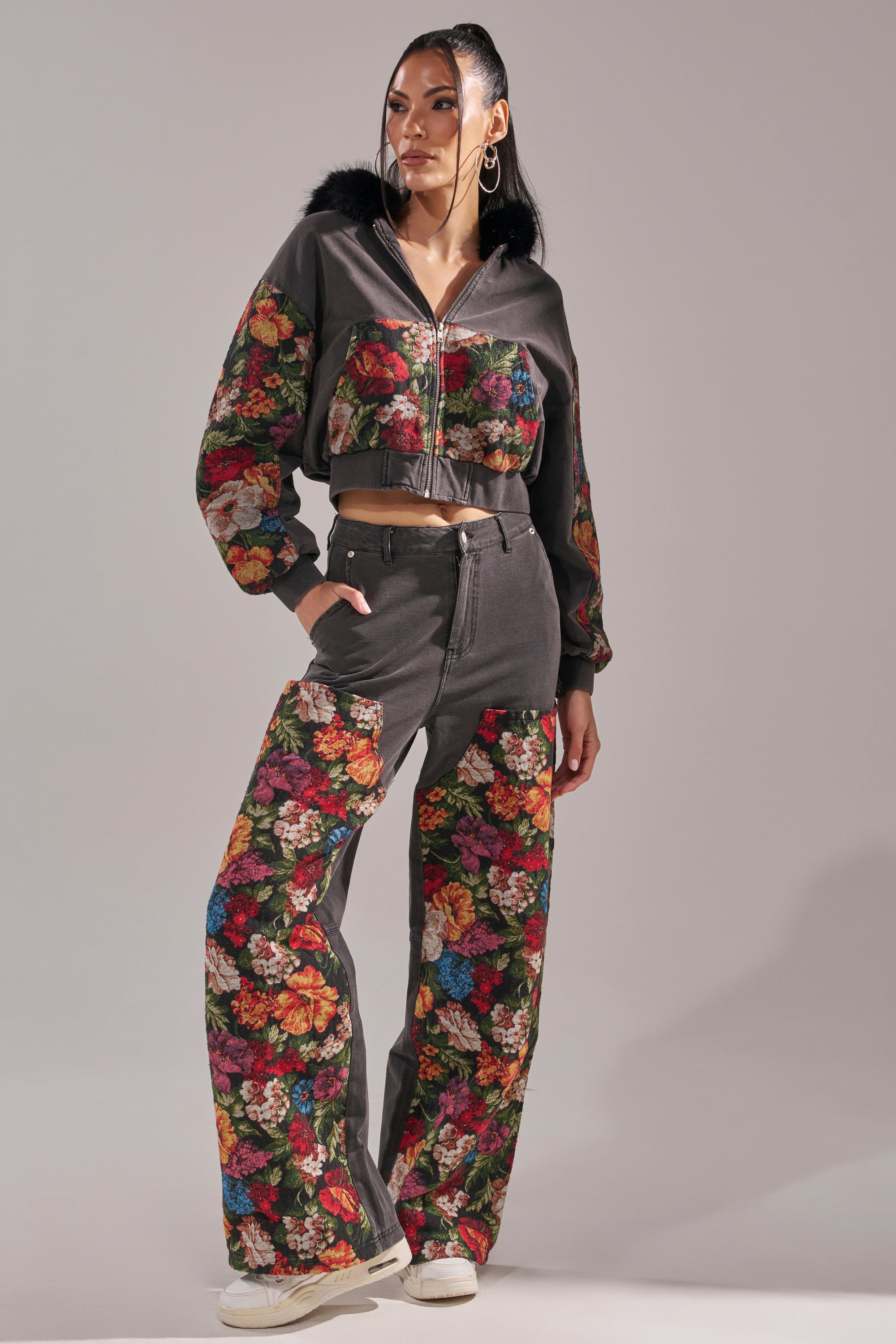 A woman models the TRY ME FLORAL DENIM—a two-piece set with a dark gray cropped zip-up hoodie and tapestry-style floral wide-leg pants—paired with white sneakers, her hair tied back and accessorized with large hoop earrings. 5