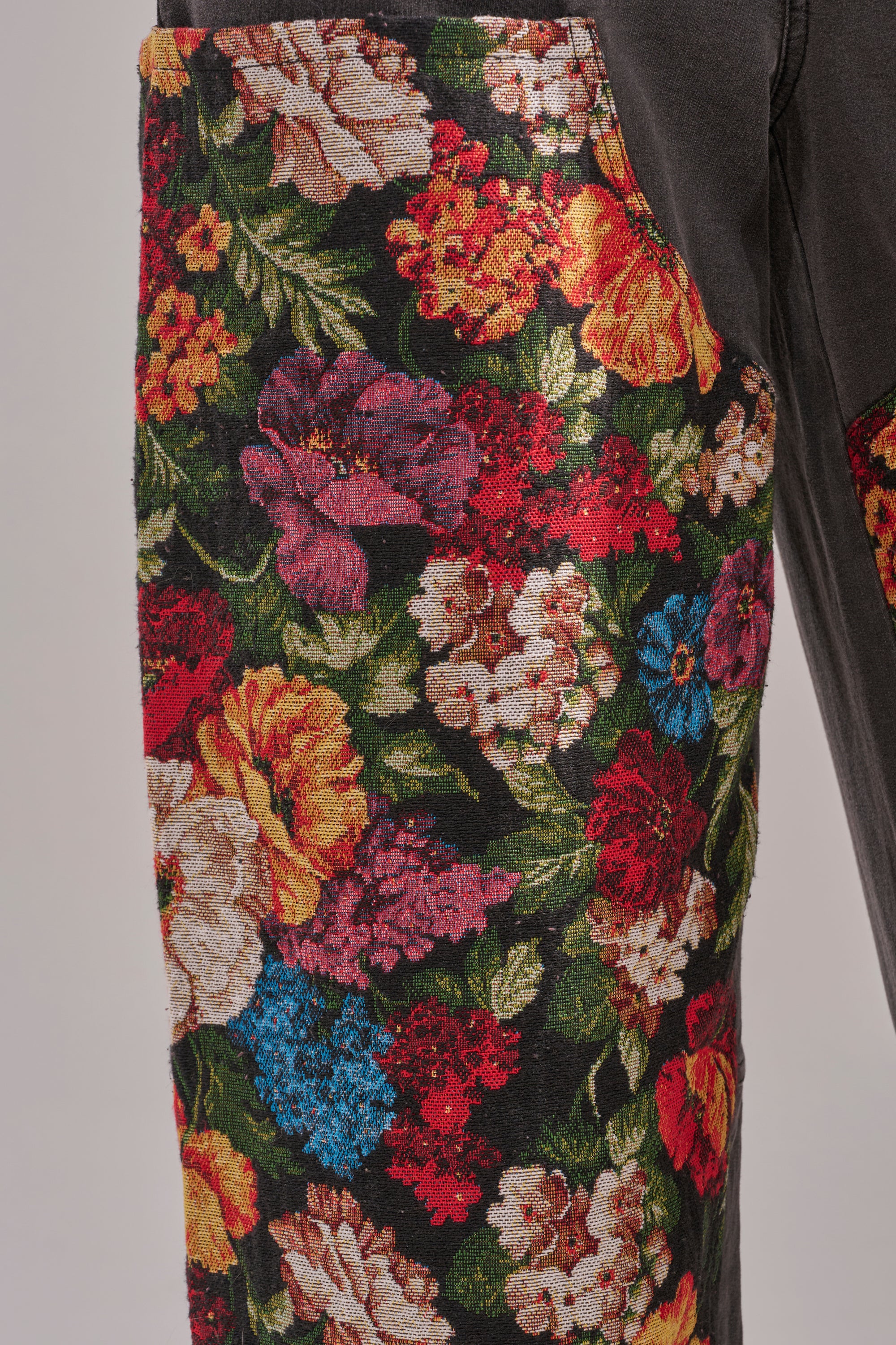 Close-up of TRY ME FLORAL DENIM: high-waisted jeans with a bold multicolored floral print—red, yellow, pink, blue, and white flowers on a dark background. 6