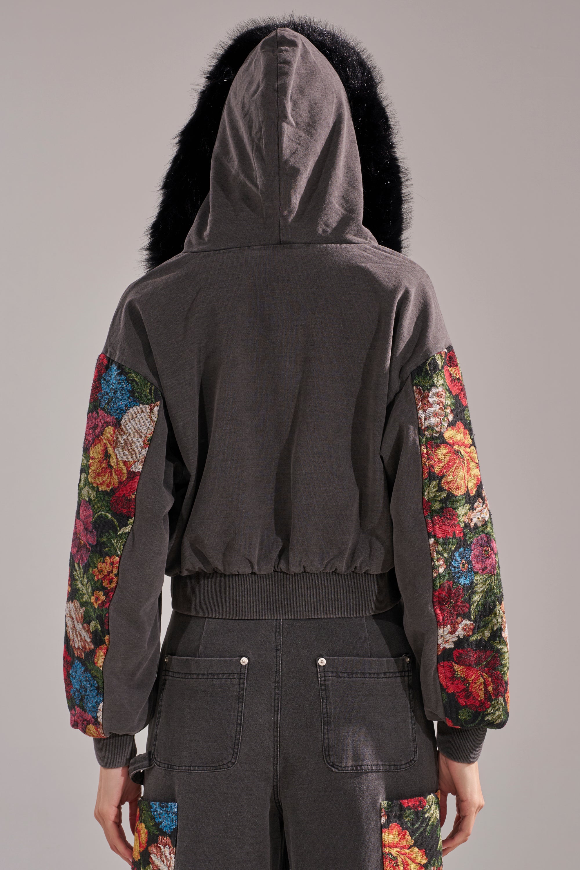 A person faces away, wearing the TRY ME FLORAL DENIM ZIP UP SWEATSHIRT with black trim and floral-patterned sleeves. The matching pants have colorful floral patches on the back pockets, set against a neutral background. 6