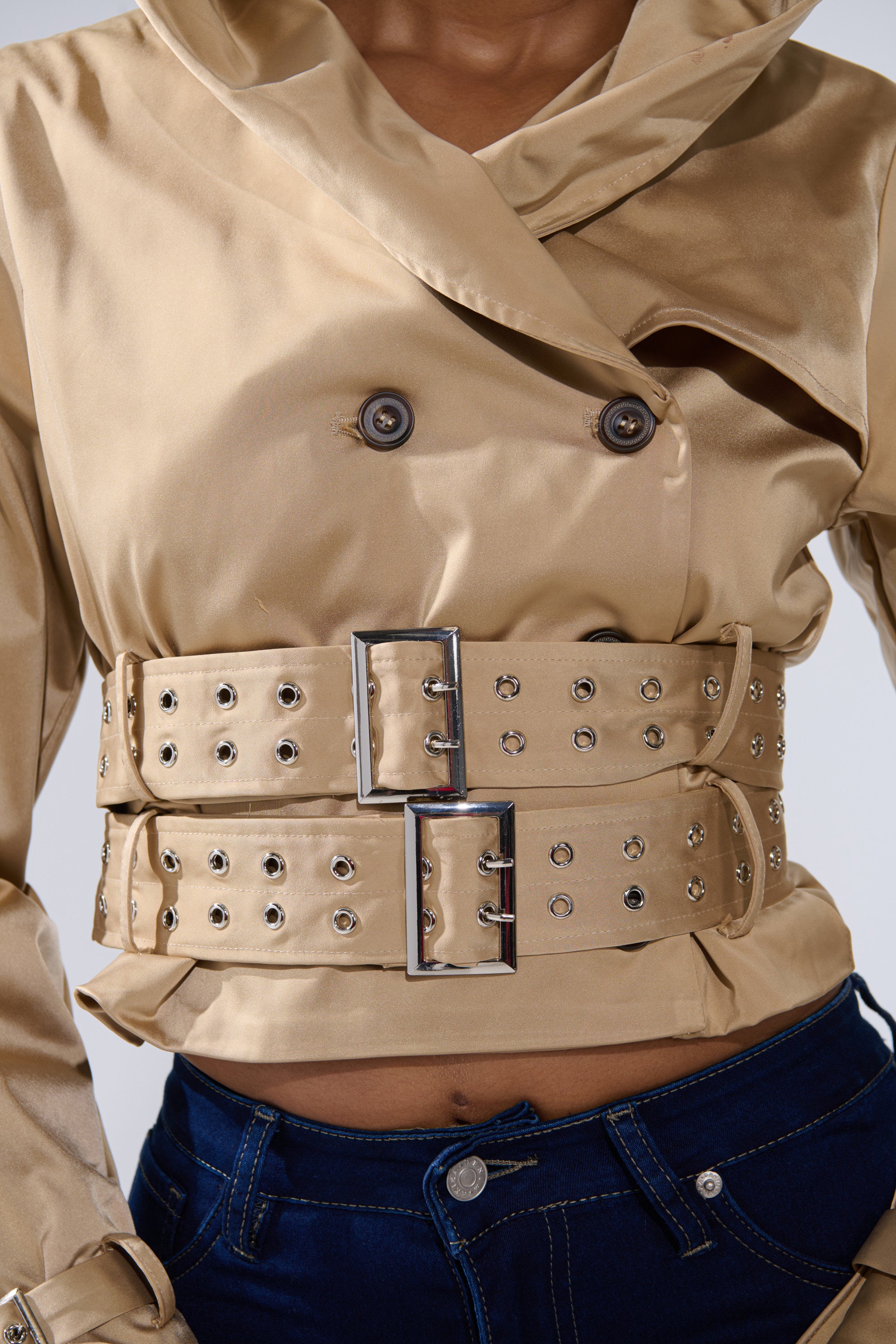 Wearing the ON DUTY CROPPED JACKET—a tan, double-breasted cropped piece with a trench silhouette, large silver buckles, belted cuffs, and grommets—paired with dark blue jeans to reveal the midriff. 9