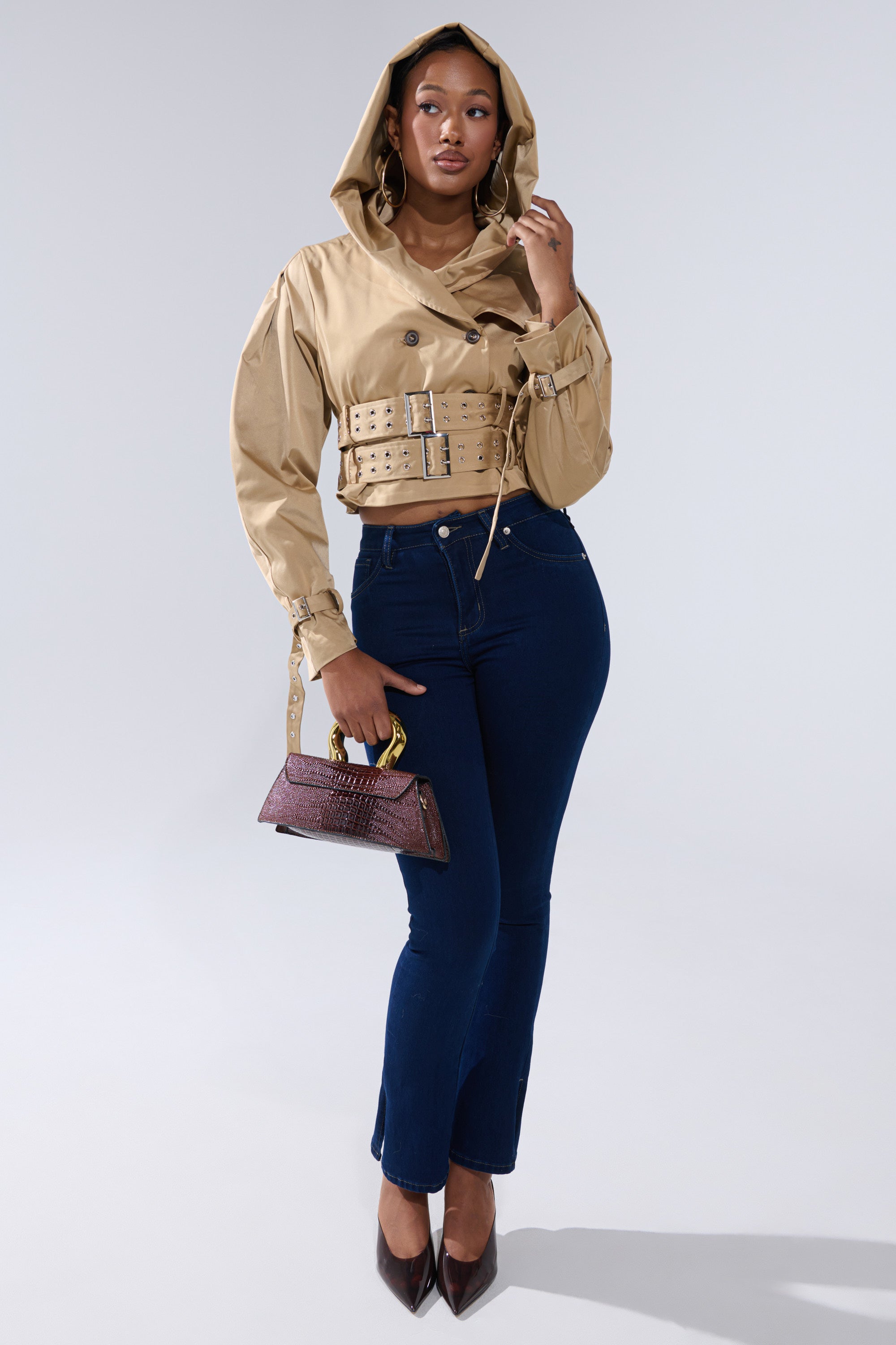 A woman models the ON DUTY CROPPED JACKET in beige, styled with dark blue jeans, dark heels, and a small purple handbag, standing against a light gray background. 8