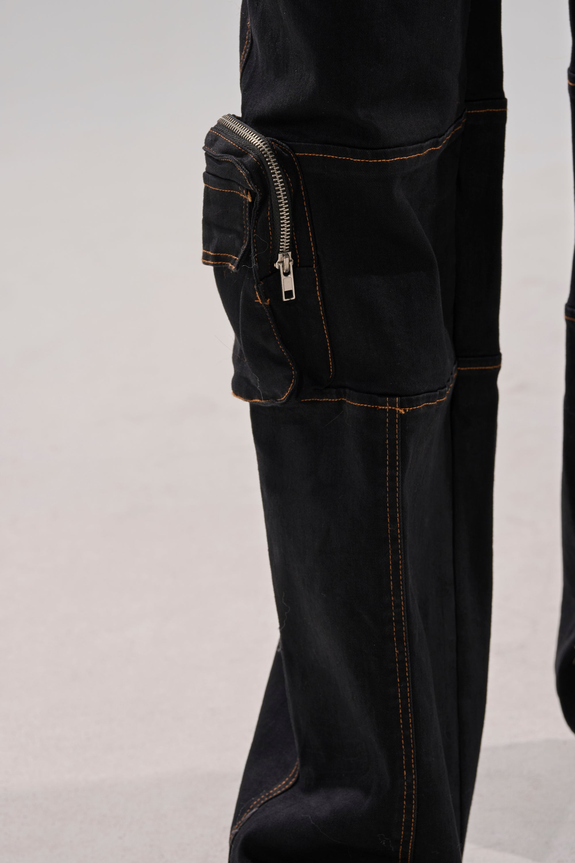 Close-up of FEELING FRISKY CARGO DENIM PANT in black with orange stitching, a large zippered thigh pocket, and a wide-leg silhouette.