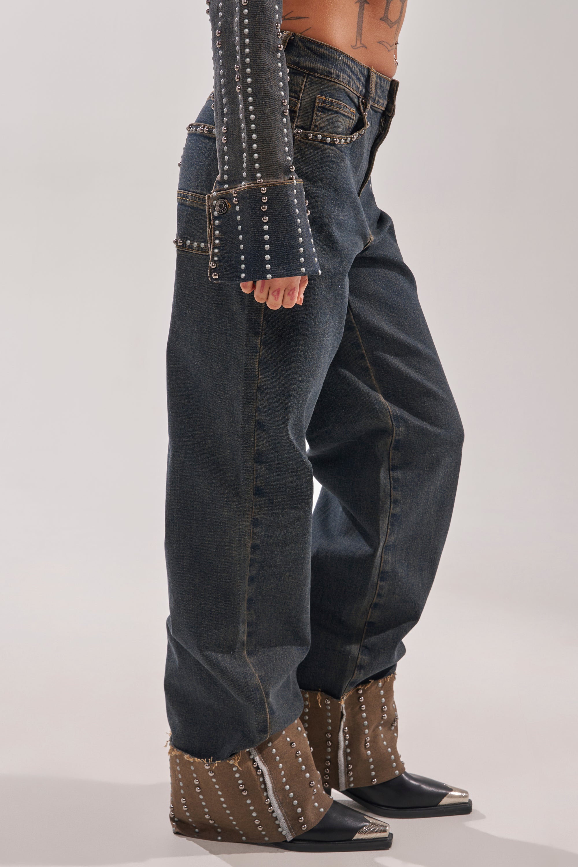 Only the lower body is visible: a person wears VANJA STUDDED WIDE LEG DENIM with silver accents, paired with brown wedge boots and a long-sleeved studded top. 3