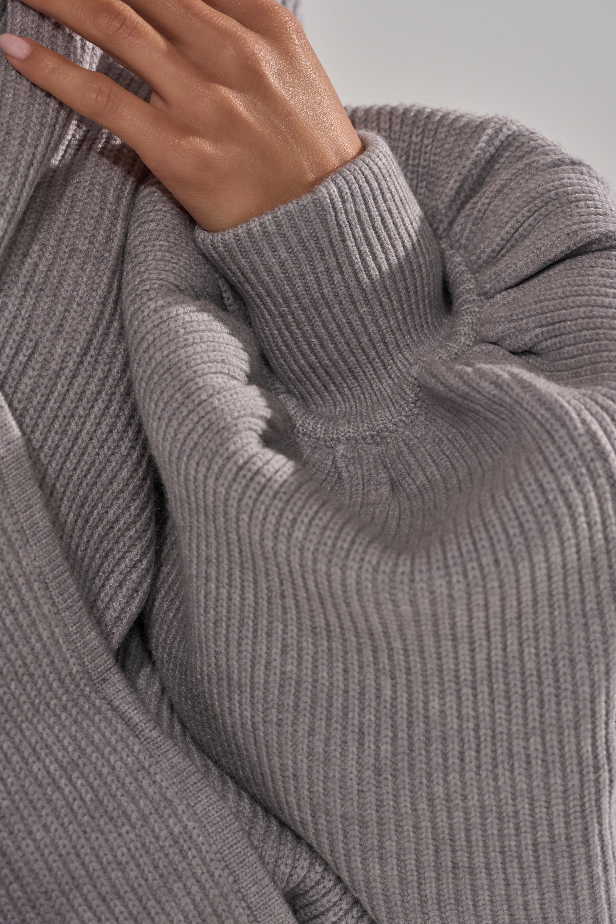 A close-up of a hand touching the collar of the CRAZY FOR YOU CROSS FRONT SWEATER, highlighting its chunky ribbed knit, heather grey color, and soft, cozy texture. 10