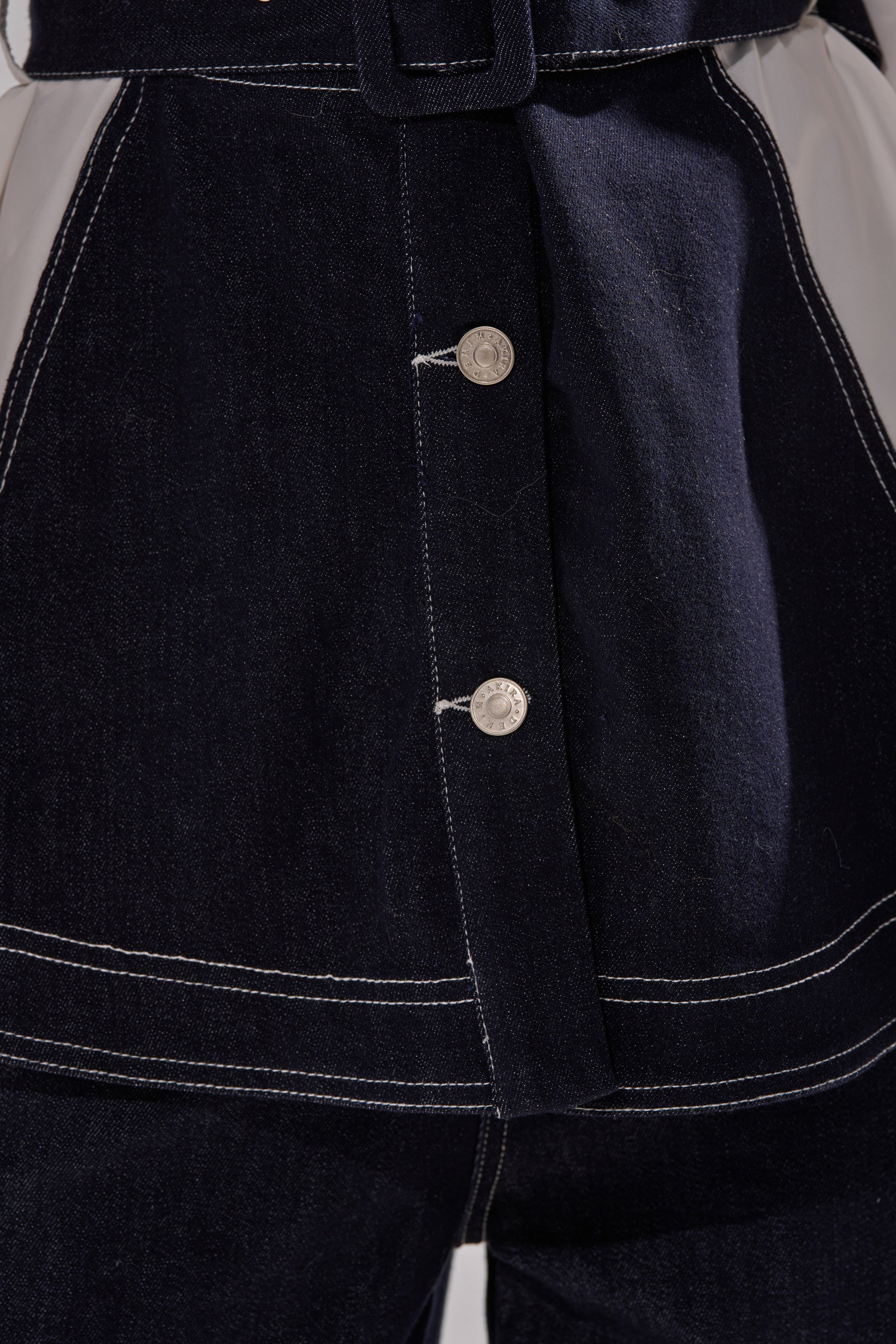 Close-up of the DIANA DENIM AND POPLIN BUTTON DOWN, showcasing dark denim with white stitching, silver buttons, light side panels, belted waist, button fly, and upper thigh detail.
