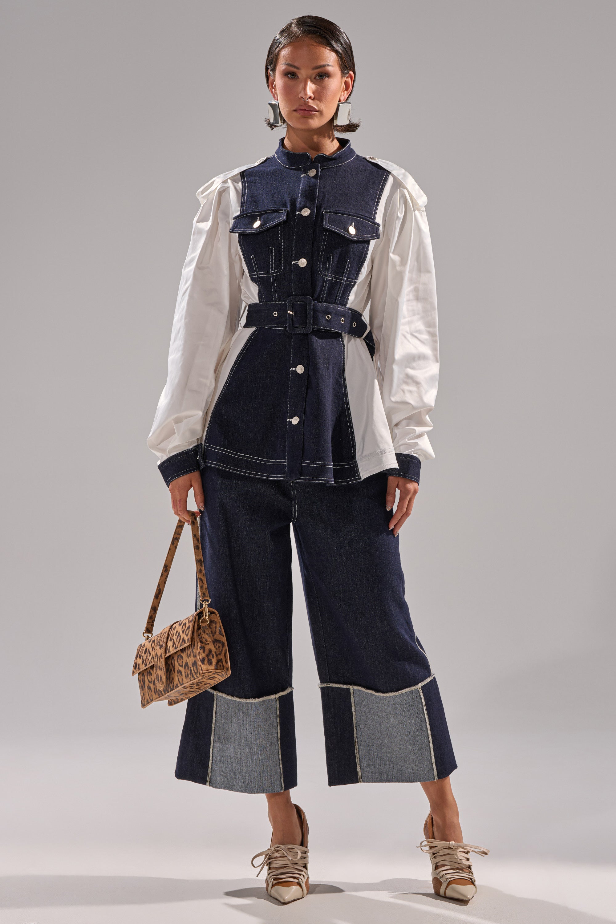 A woman wears the DIANA DENIM AND POPLIN BUTTON DOWN, styled with matching wide-leg denim pants, a leopard print handbag, and beige lace-up shoes against a plain light gray background.