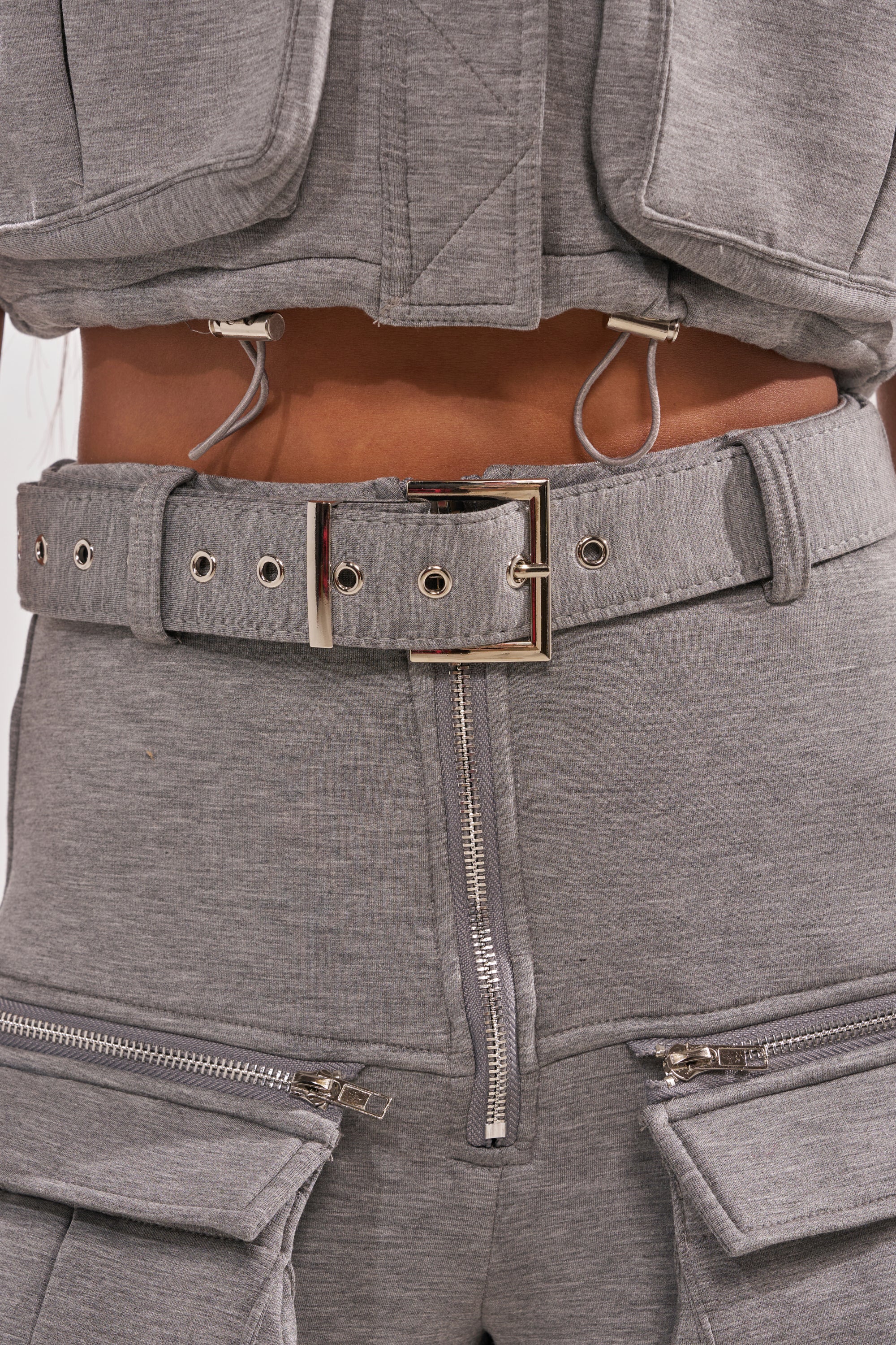 Close-up of a person wearing the THAT GIRL SCUBA CARGO PANT, a grey high-waisted cargo pant with zippers, belted style, and exposed elastic details for a streetwear-inspired look. 7