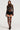 A person is styled in the MOMENTS IN TIME GLOVED LACE BODYSUIT, showcasing corset detailing with a sheer long-sleeve top, high-waisted shorts, and thigh-high stockings. They finish the outfit with platform sandals and wear their hair long and straight against a simple, light-colored backdrop.