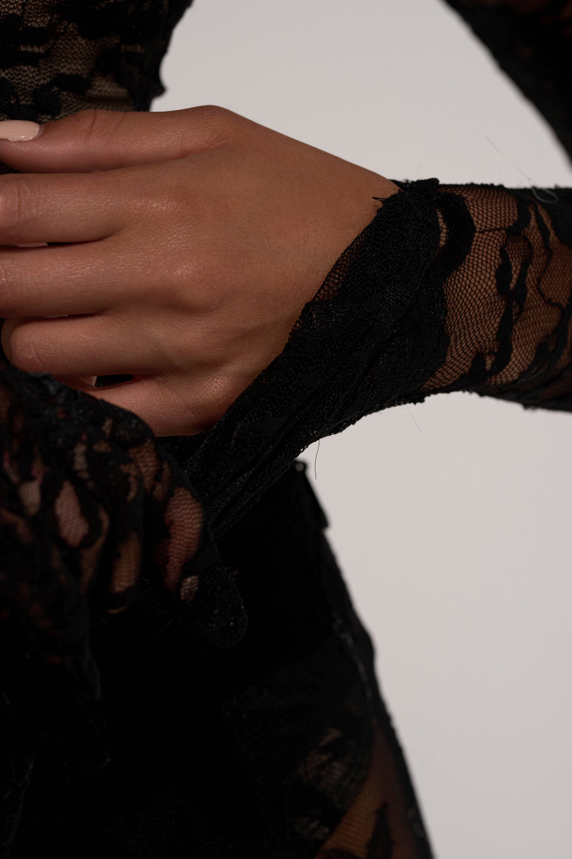 A close-up of a hand resting on the waist, clad in the ALL THE ATTENTION LACE GLOVE BODYSUIT, featuring delicate black lace sleeves against a plain light background.