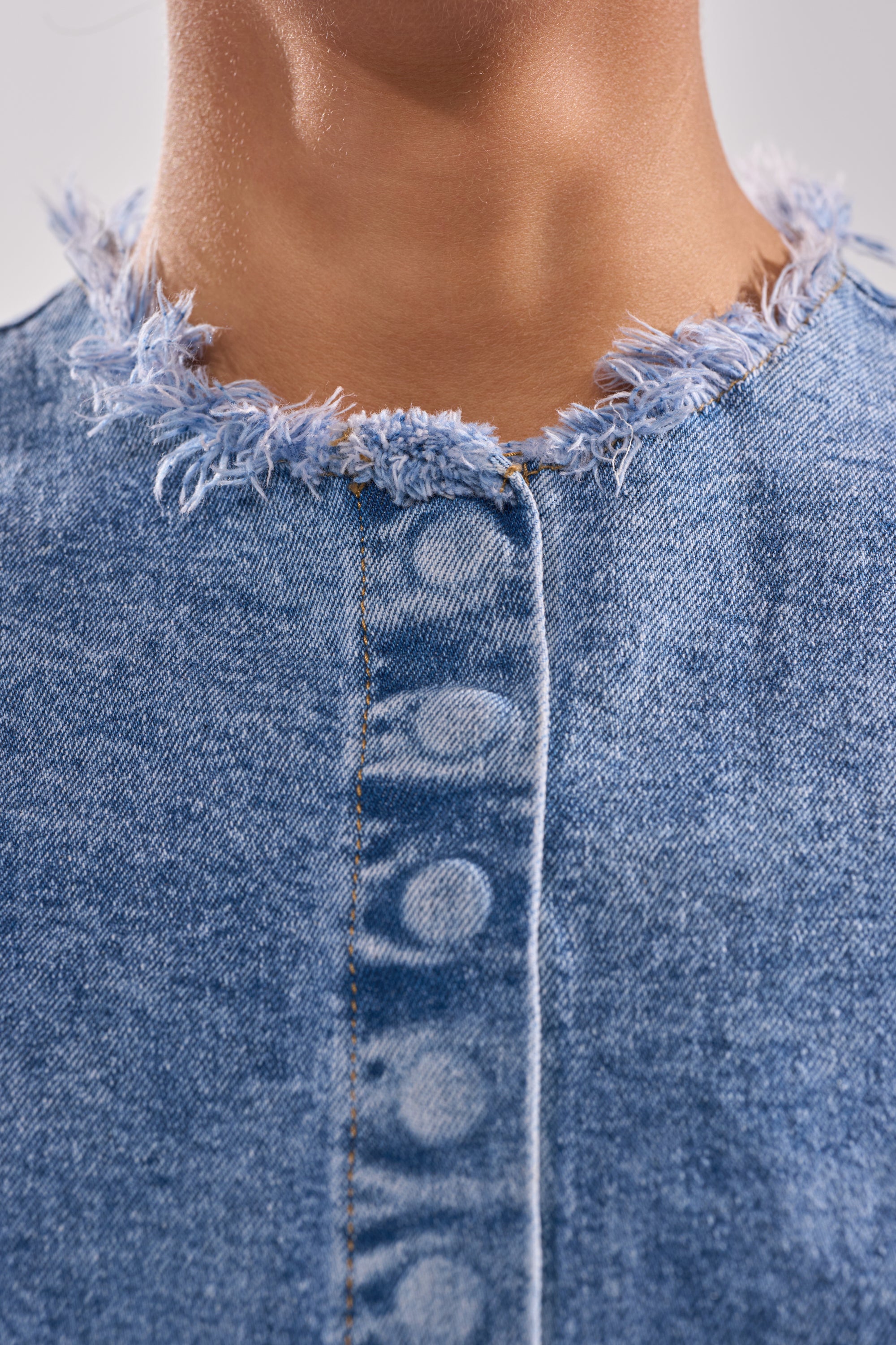 Close-up of a person's neck wearing the DONT PLAY WITH MY HEART DENIM BLOUSE, showcasing its frayed, unfinished neckline, visible seam, and faded button marks for a distressed look.