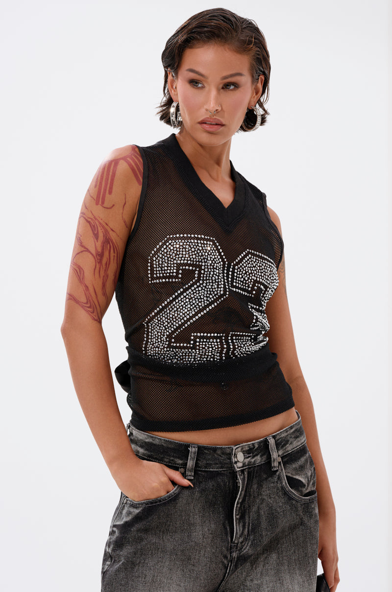 A person with short slicked-back hair wears the TWENTY THREE TANK, featuring a rhinestone #23, paired with faded black jeans and hoop earrings. They have a red abstract arm tattoo and pose confidently with one hand in their pocket.