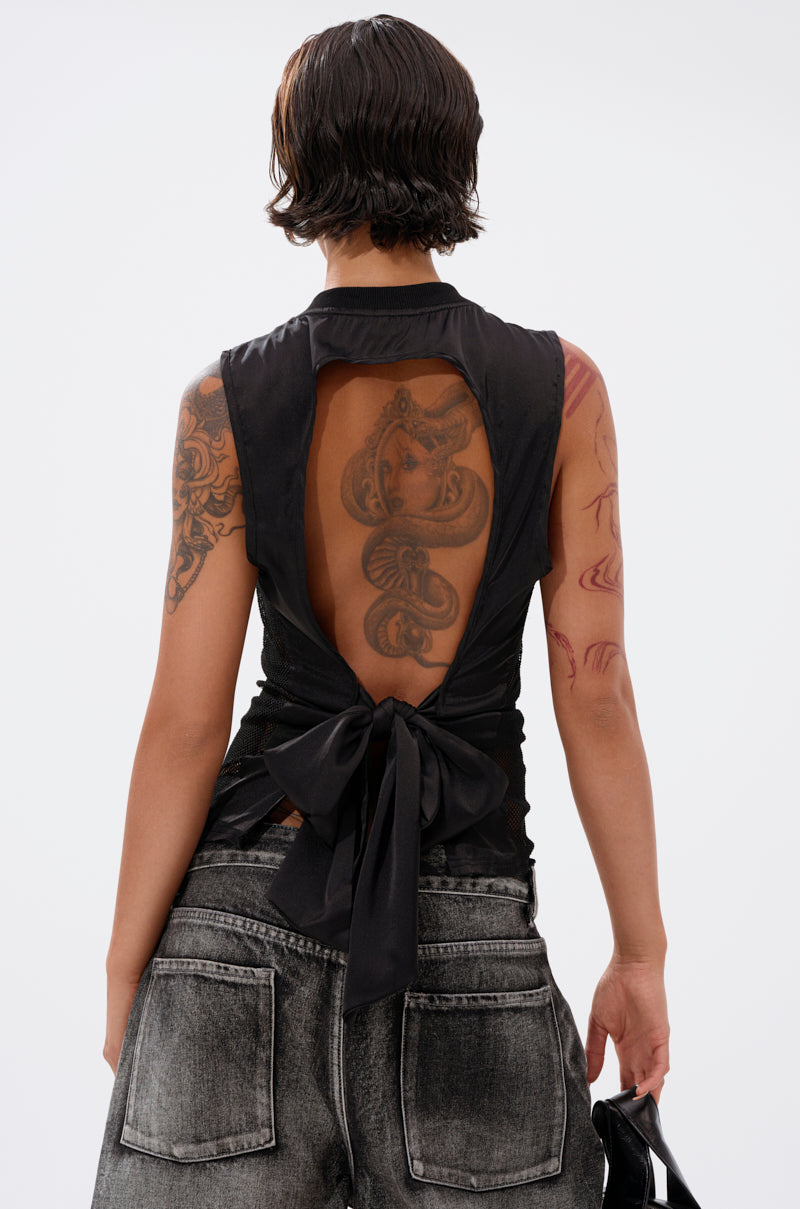 A person with short dark hair and arm tattoos is seen from behind wearing the TWENTY THREE TANK, a sleeveless mesh top with an open back and bow, paired with faded black jeans that reveal a large snake tattoo. 4