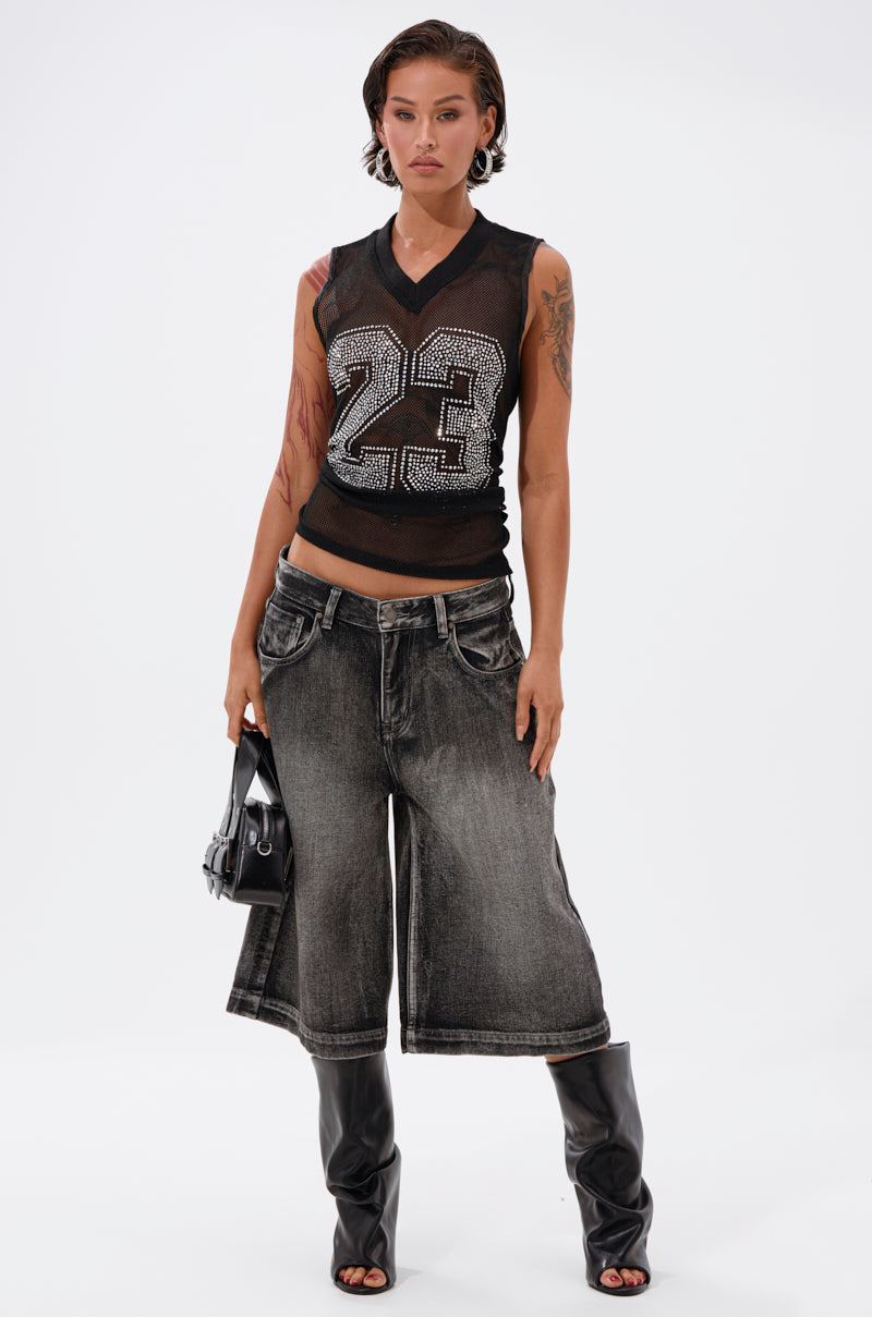 A person stands confidently in the TWENTY THREE TANK, a black mesh jersey-inspired top featuring a glittery rhinestone varsity 23 on the front, paired with wide-leg faded denim shorts, black knee-high boots, and a small black handbag. 5