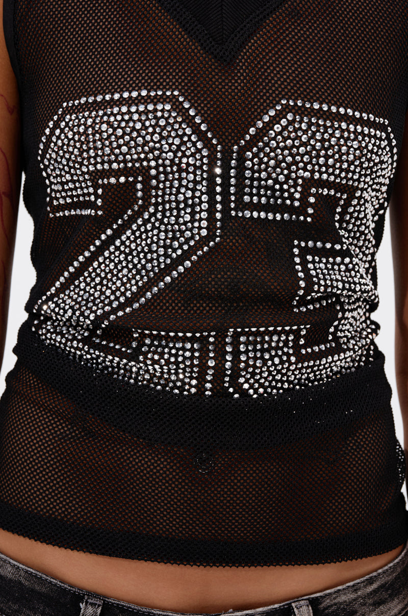A close-up of someone wearing the TWENTY THREE TANK, a black mesh tank top with rhinestones forming "23." The image focuses on their midsection and faded jeans, showcasing the jersey-inspired design. 7