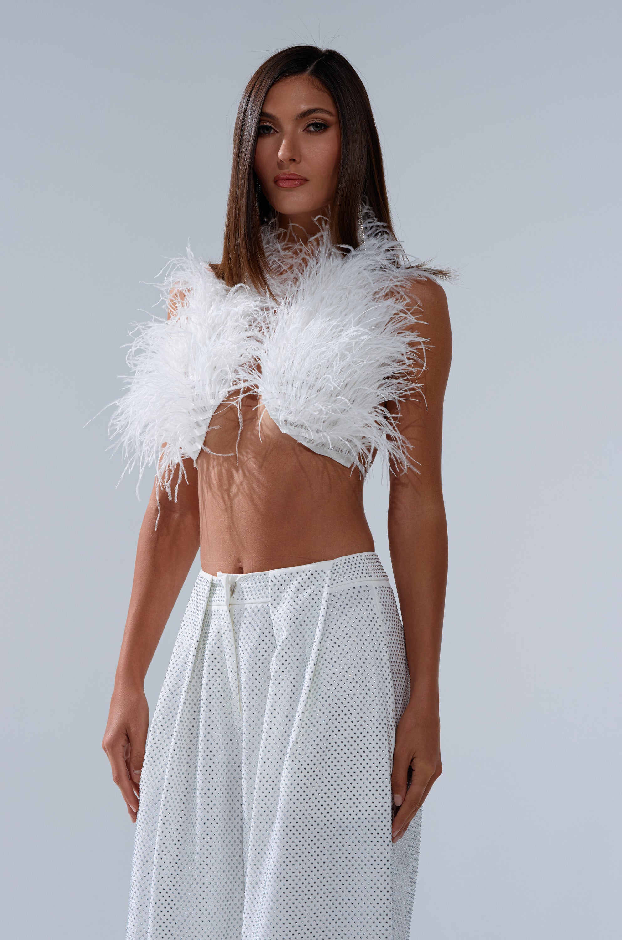 A woman with straight brown hair models the SHAKE IT FOR ME GIRL FEATHER BRALETTE and high-waisted, wide-leg sheer mesh white pants, standing against a plain light gray background. 3