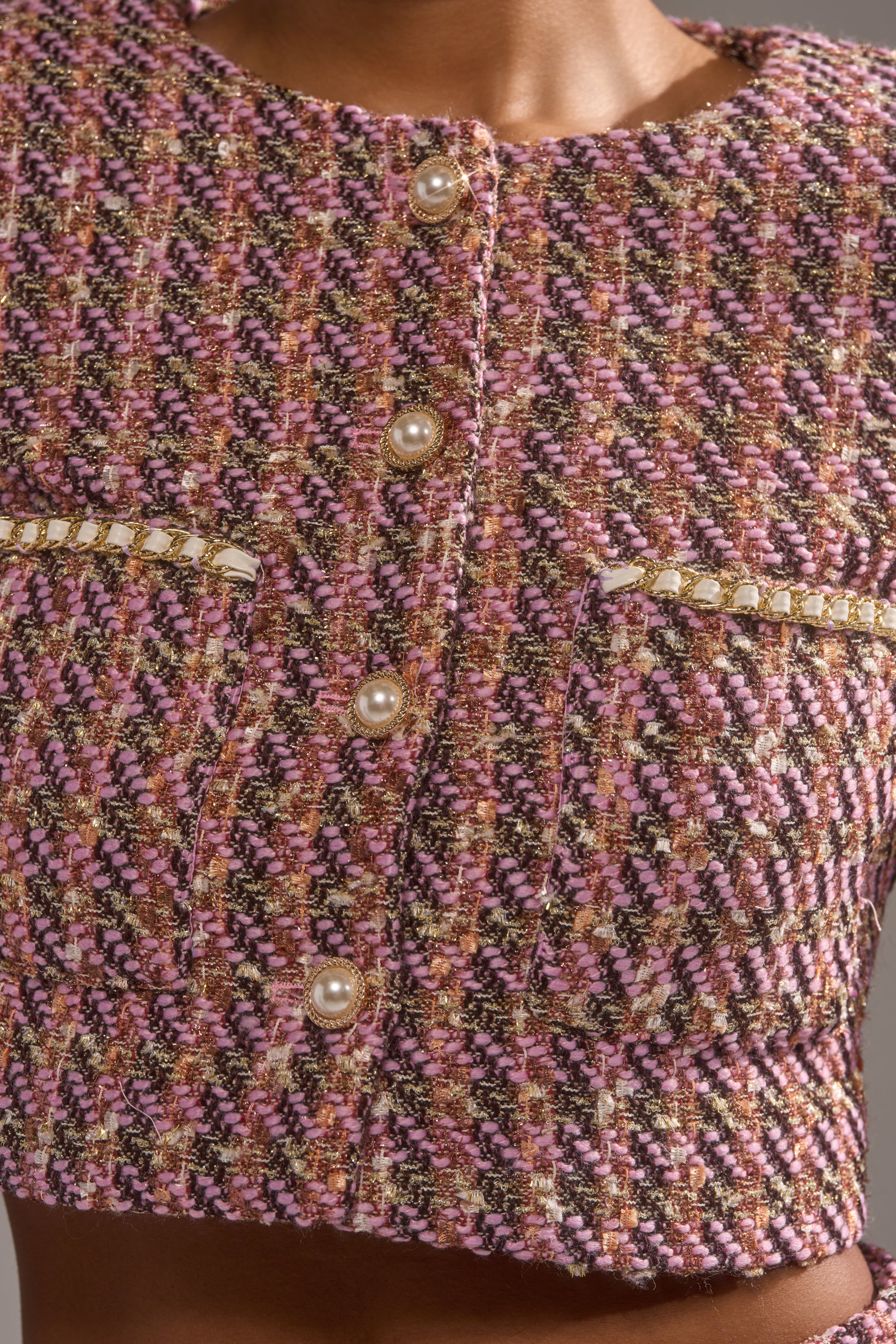 Close-up of the TRUTH OR DARE TWEED BLAZER in pink, brown, and gold hues, showcasing pearl buttons and decorative pocket flaps with metallic details and pearl accents. 7