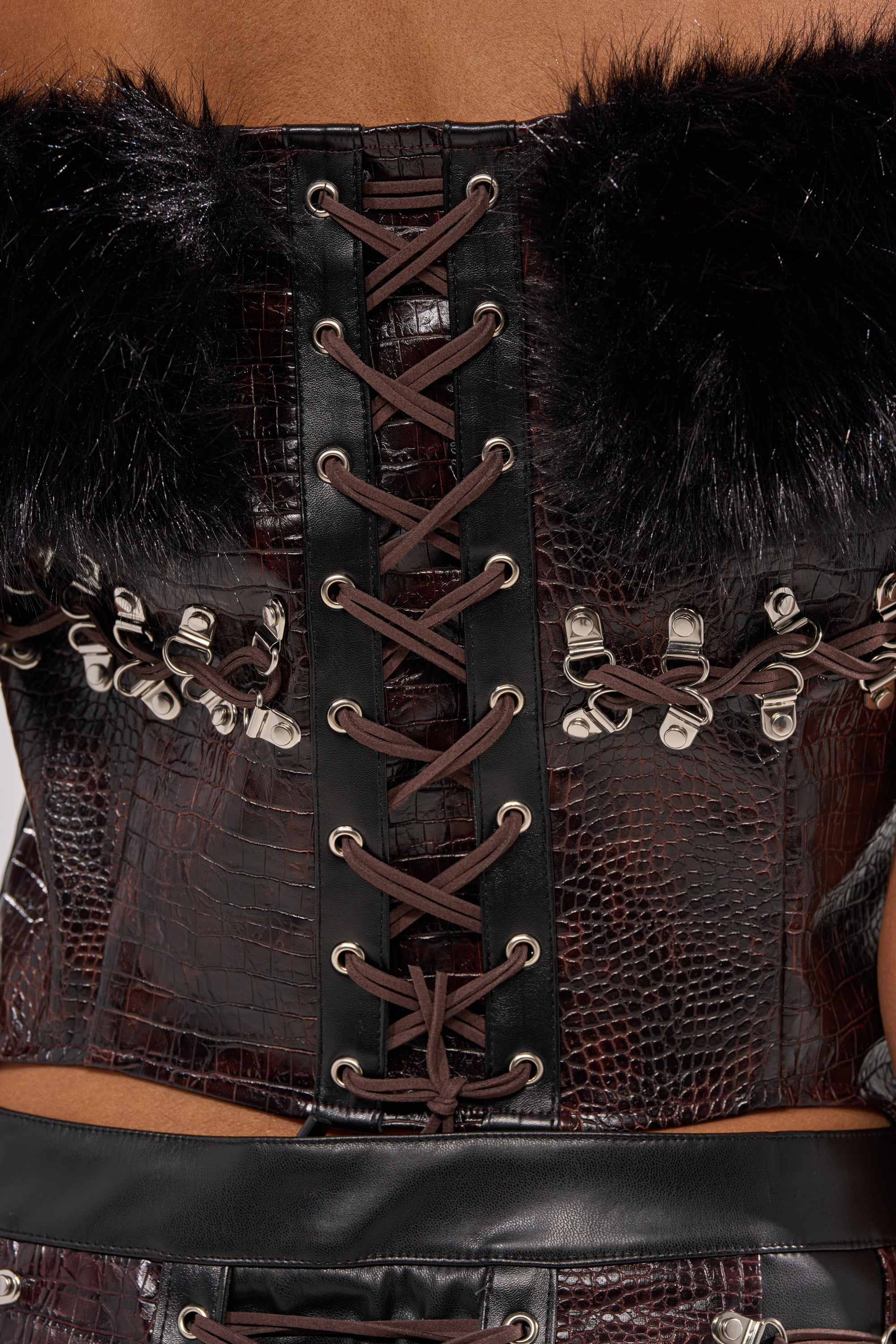 Close-up of the back of the TOO SEXY FOR YOU CORSET in dark brown faux leather with black faux fur trim, silver eyelets, and black criss-cross laces. 7