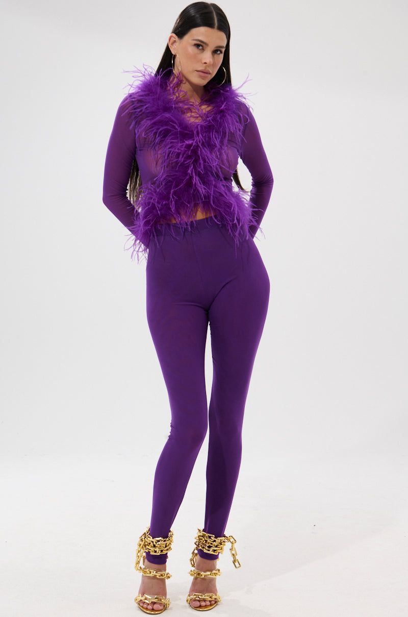 A woman stands against a plain background wearing a vibrant feathered top with PUMPED UP MESH LEGGING in purple and gold heeled sandals featuring chunky chain details. 0