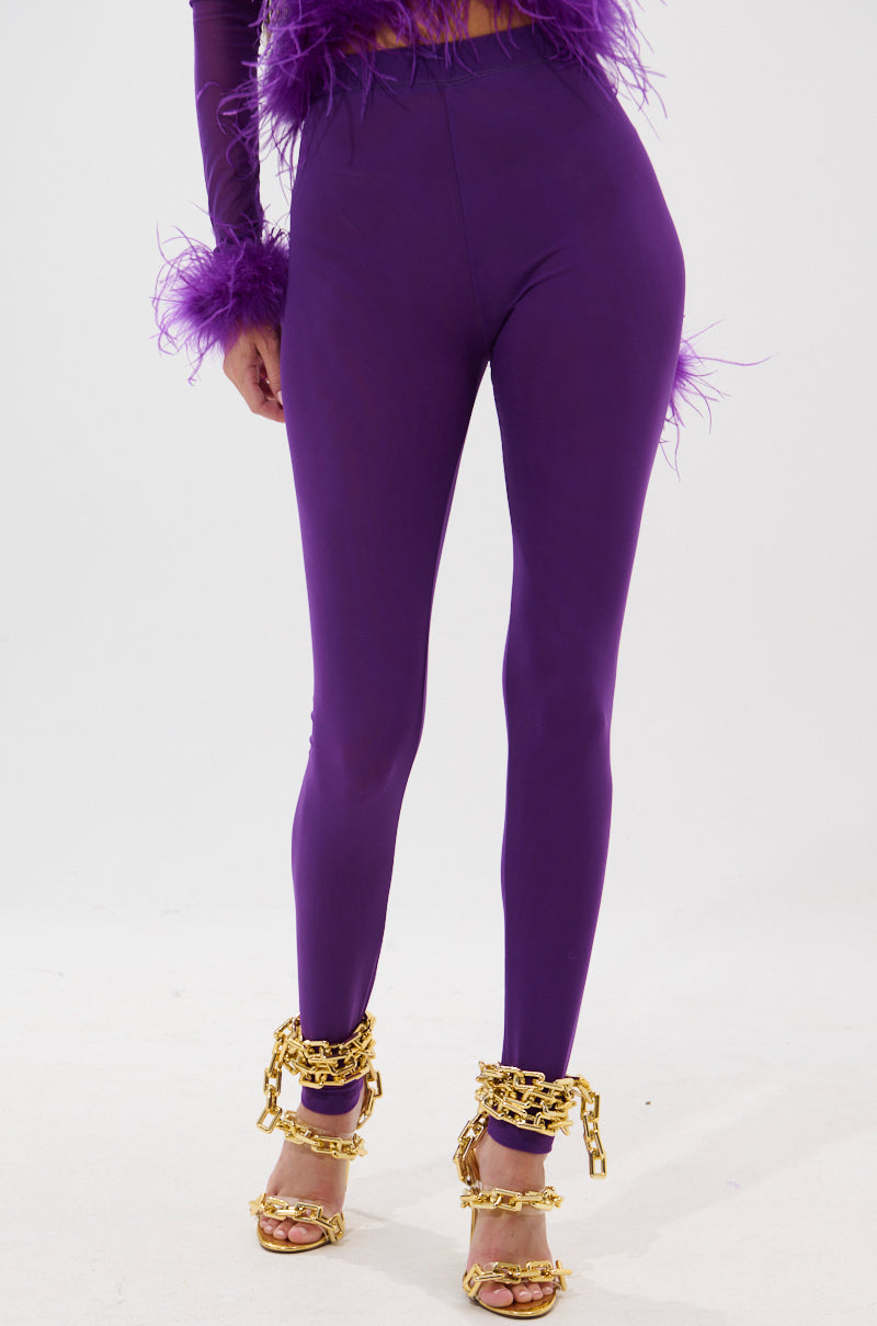 A person wears the PUMPED UP MESH LEGGING in royal purple with a matching feather-detailed top and gold high-heeled sandals featuring thick gold chains, standing against a plain white background. 2