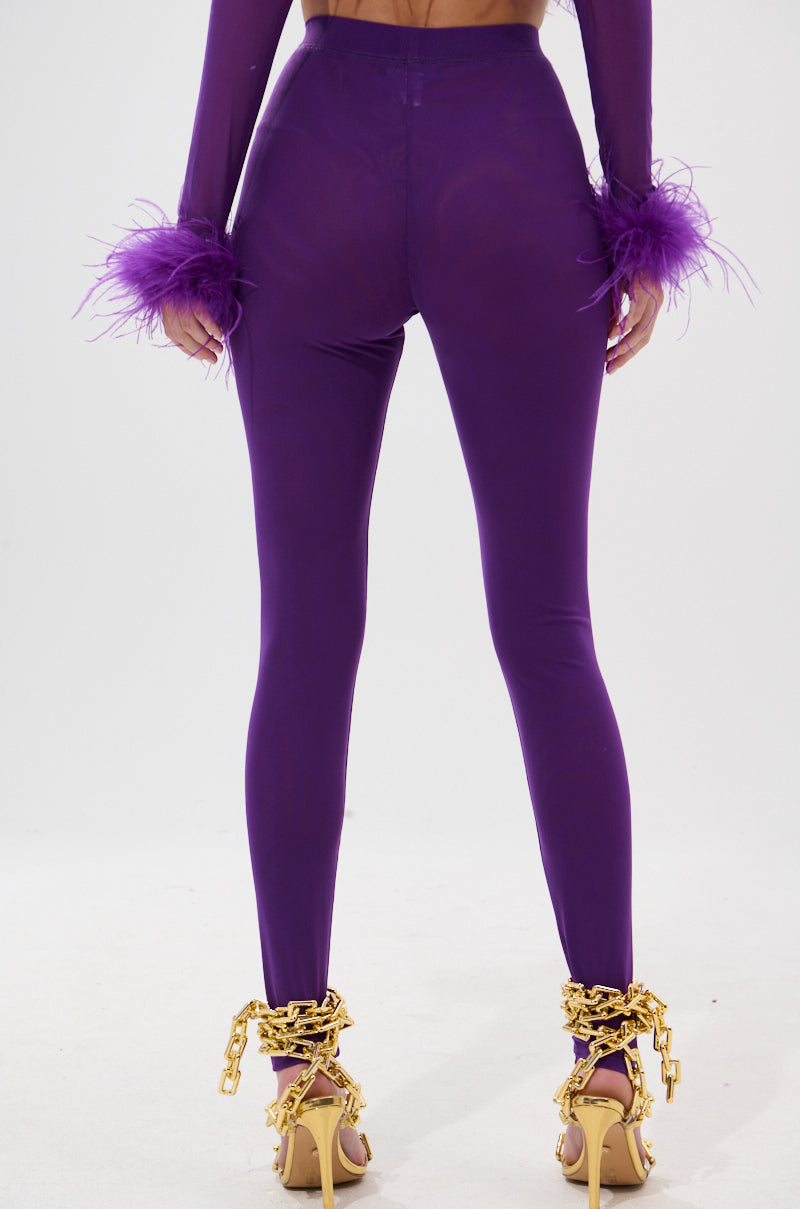 A person shown from the back wears PUMPED UP MESH LEGGING in royal purple with feather details at the wrists and gold chain-embellished high-heeled sandals, set against a plain background. 4