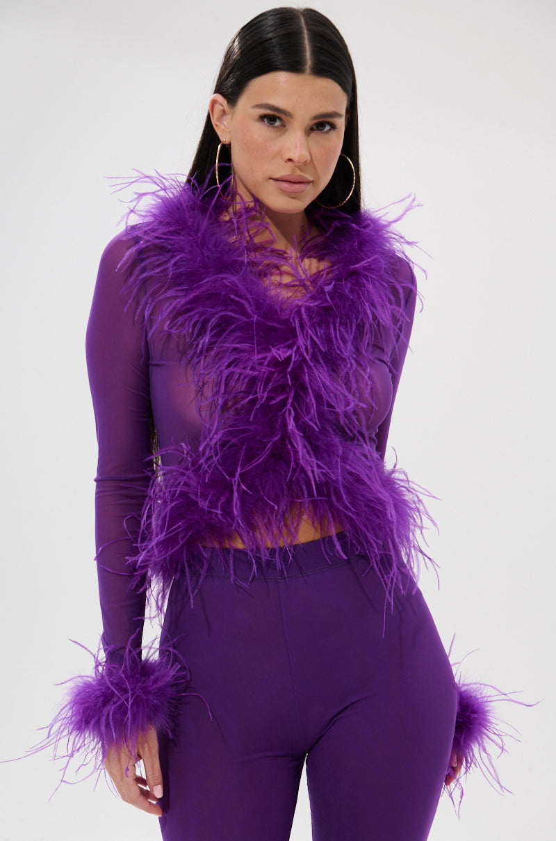 Model wears the PUMPED UP FEATHER BLOUSE, a sheer mesh top with fluffy purple feather trim on the collar and cuffs, paired with matching pants, posing against a plain white background.