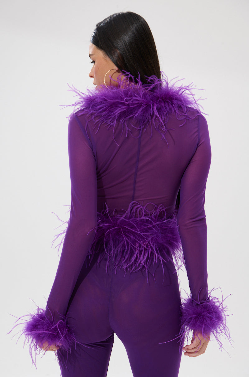 A woman faces away, wearing the PUMPED UP FEATHER BLOUSE—a sheer mesh top with feathery purple trim on the collar, waist, and cuffs—set against a plain light background.