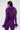 A woman faces away, wearing the PUMPED UP FEATHER BLOUSE—a sheer mesh top with feathery purple trim on the collar, waist, and cuffs—set against a plain light background.