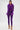 A woman poses against a white background in the PUMPED UP FEATHER BLOUSE, a vibrant purple top with feather trim on the sleeves, paired with gold high-heeled sandals adorned with bold chain accents.