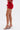 A person in the FIERCE MESH MINI SKIRT and a matching red mesh top with feathered sleeves stands in profile, wearing strappy gold heels. The curve-hugging look pops against a plain white background.